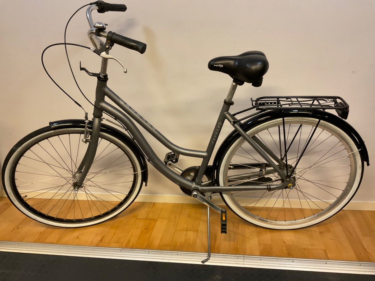 Grå Monark stadscykel med svart sadel, vita däck och pakethållare