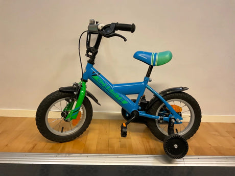 Blå och grön barncykel med stödhjul och tjocka däck på inomhus golv