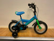 Blå och grön barncykel med stödhjul, svart kedjeskydd och skärmar
