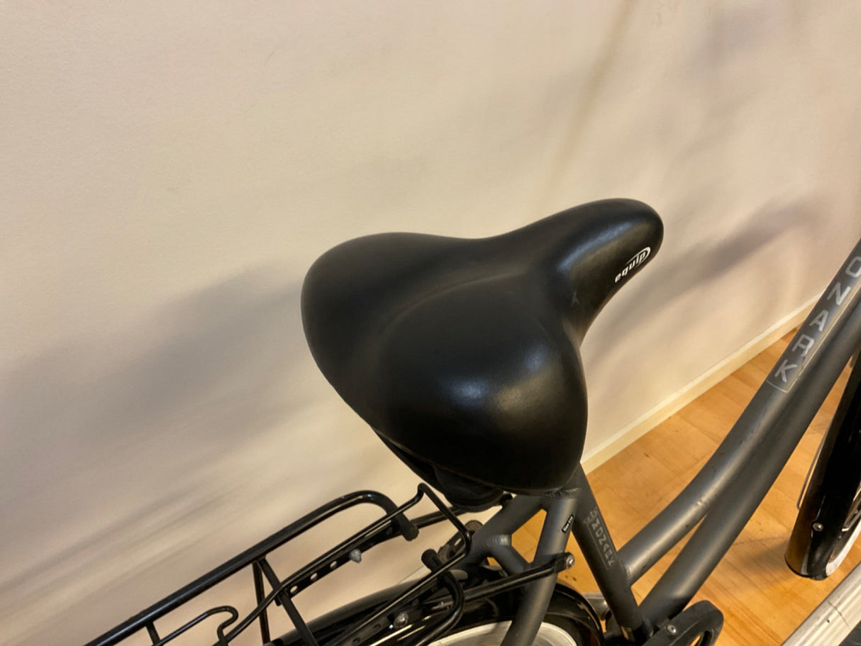 Svart cykelsadel av märket Equip på grå cykel med pakethållare och trägolv