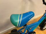 Blå och grön cykelsadel med vita ränder och texten Biltema på blå barncykel